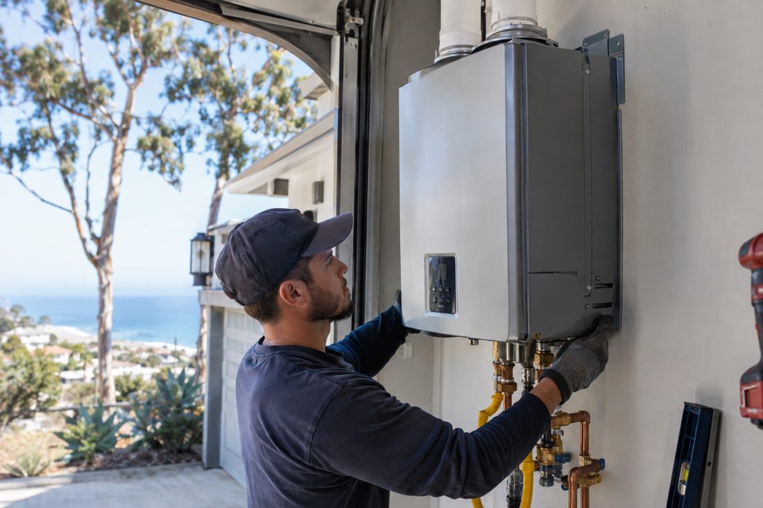 A tankless water heater being mounted on a garage wall at a coastal Encinitas home with eucalyptus trees in Encinitas, CA